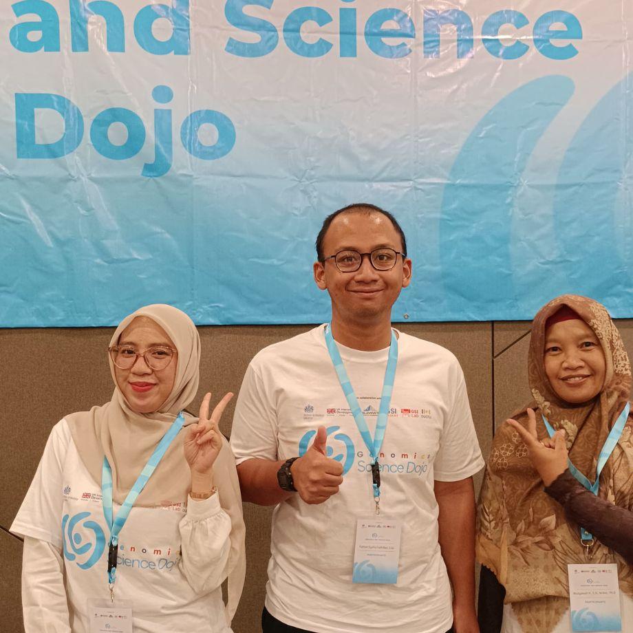 Ariantika with two fellow participants in front of a Genomics Science Dojo banner at a bioinformatics workshop